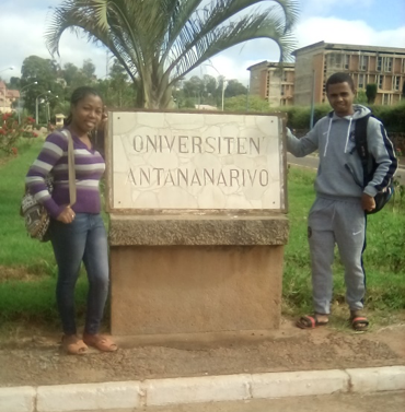 two Malagasy students standing next to University of Antananarivo sign