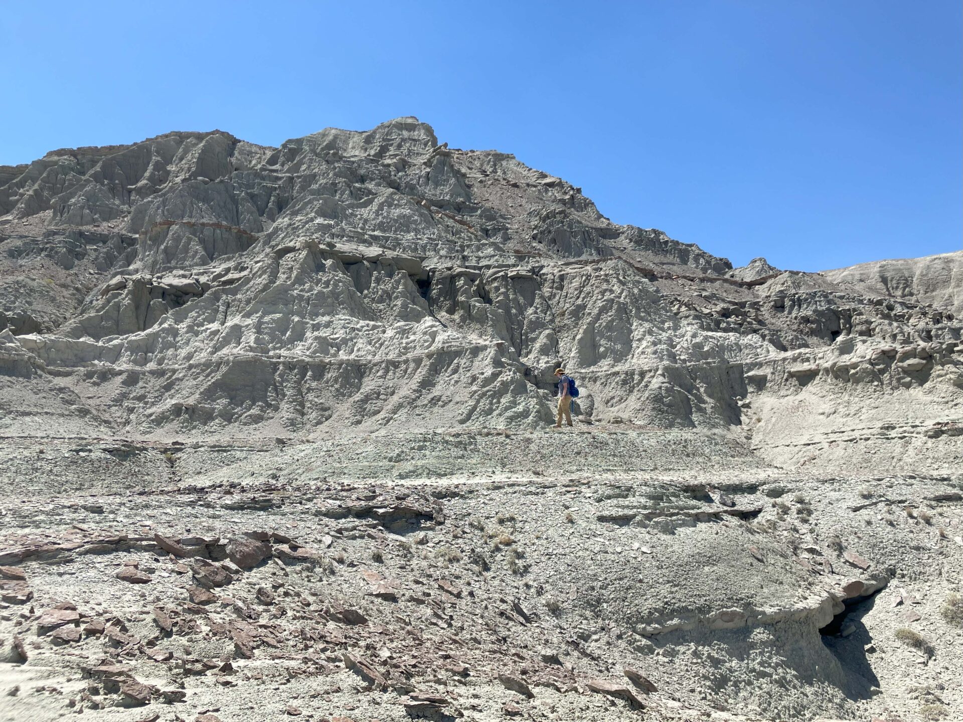 A paleontologist dressed in field gear is barely visible against the backdrop of a gray rocky cliff face in Wyoming.