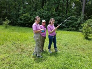 Three women standing in field in pink shirts holding radio telemetry equipment