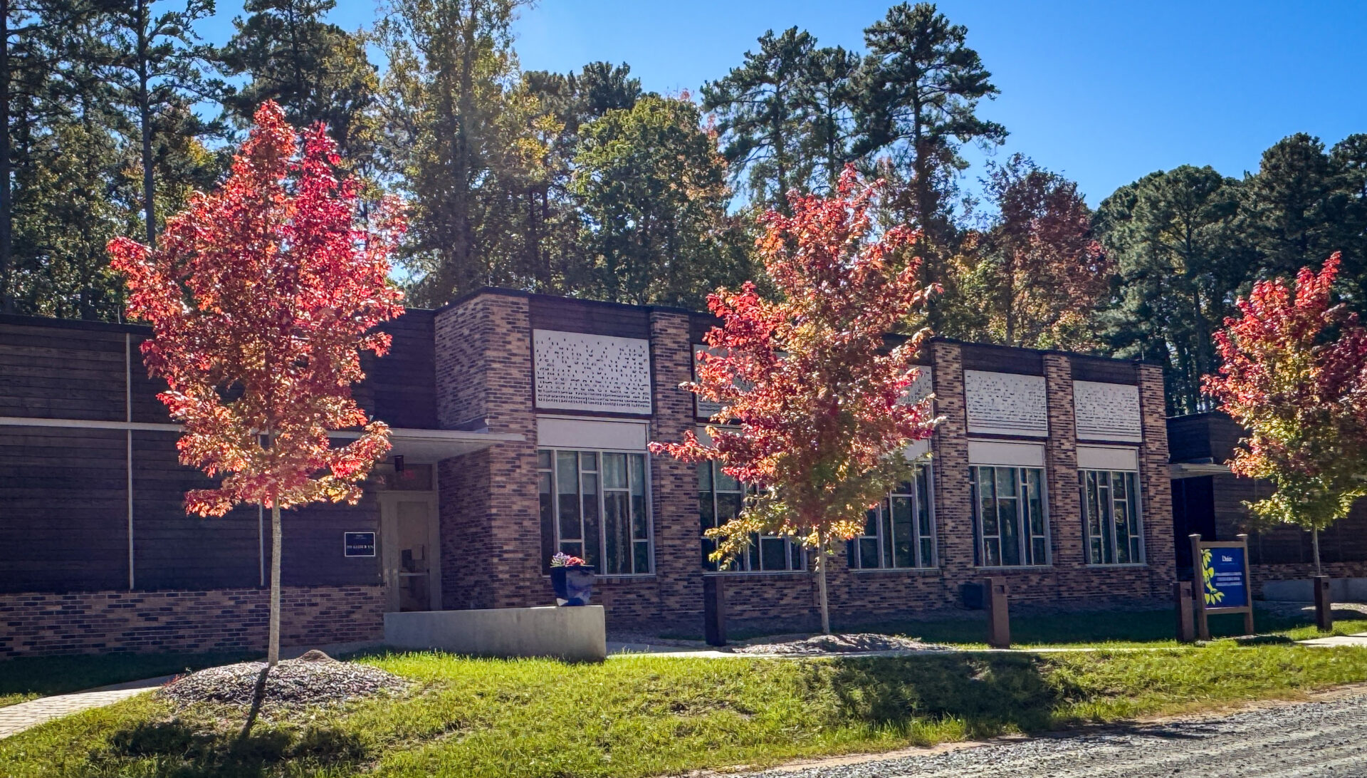 A large, one-level brick building during an autumn afternoon, with red-leafed trees in the foreground.