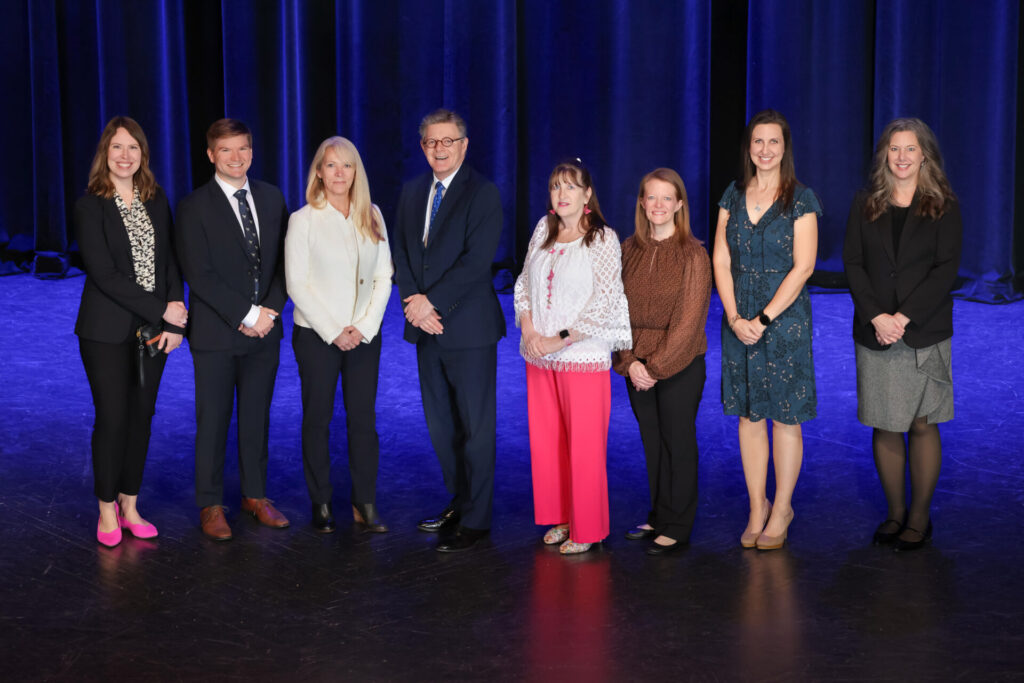 Eight members of DLC management team stand on a stage at the Awards Ceremony
