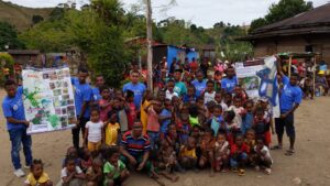 A group of Malagasy children pose with adults in Duke shirts who are holding DLC posters with maps and info about lemurs